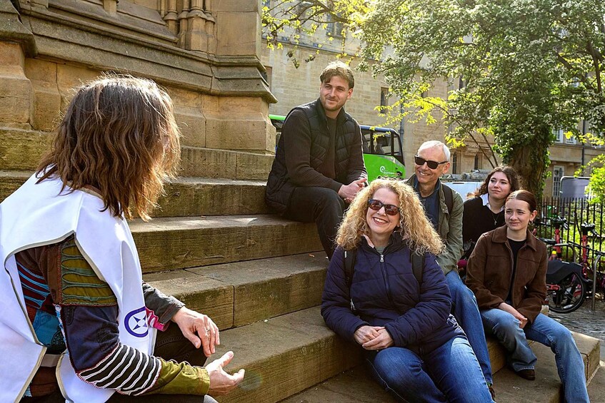 A group of people sitting on stone steps in an outdoor setting with trees and buildings in the background. 2