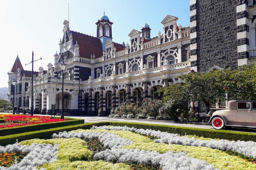 A historic building with ornate architecture, a garden with various flowers, and a vintage car. 2