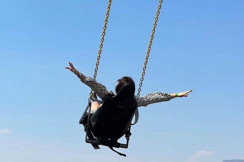 A person on a swing with outstretched arms against a clear sky. 5