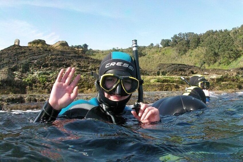 Dos personas haciendo snorkel en un cuerpo de agua con terreno rocoso y vegetación al fondo. 5