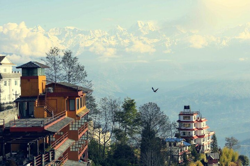 A mountainous landscape with buildings, a bird in flight, and snow-capped peaks in the background. 3