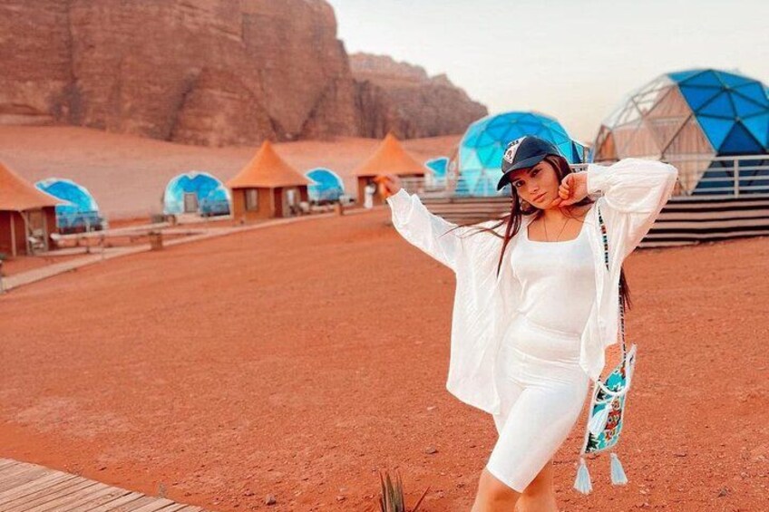 A desert landscape with red soil, a person in white attire, and blue-domed structures in the background. 2