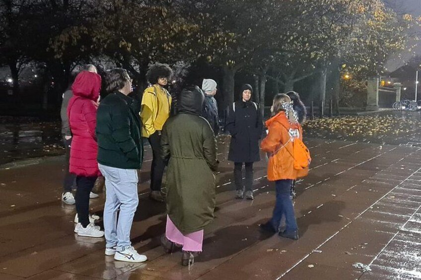 A group of people standing on a wet pavement at night. 3
