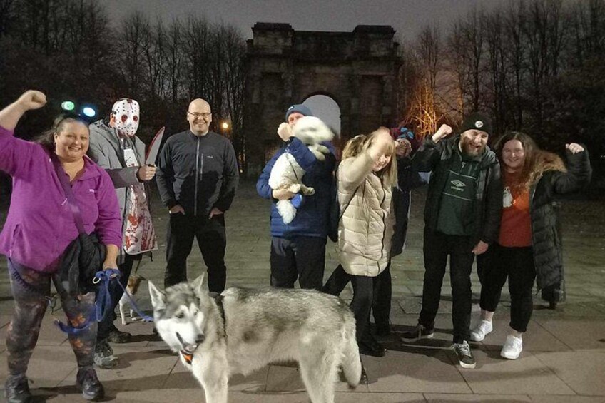 A group of people posing with a husky dog in an outdoor setting with a historic building in the background. 2