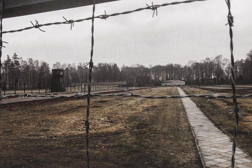 A fenced area with a watchtower, a paved path, and a building in the distance. 4