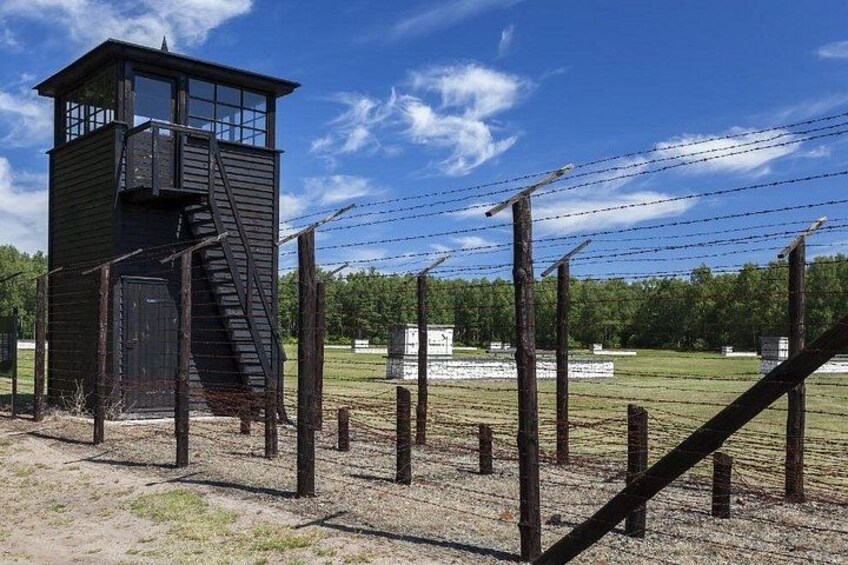A watchtower, barbed wire fence, and a grassy field. 1