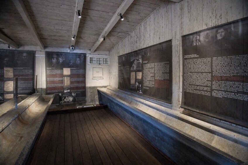 A dimly lit room with wooden benches, stone walls, and informational plaques. 2