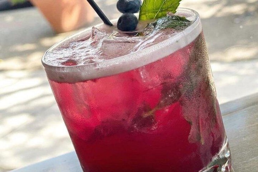 Ein Glas rotes Getränk mit Eiswürfeln, einem schwarzen Trinkhalm und einer Minzblatt-Garnitur. 5