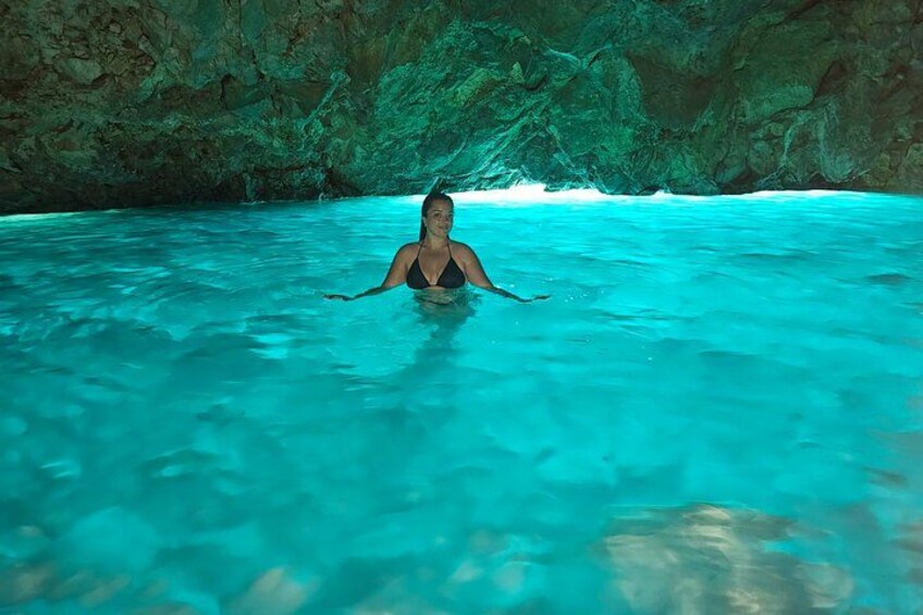 A person in a black swimsuit in clear turquoise water with rocky cliffs in the background. 1
