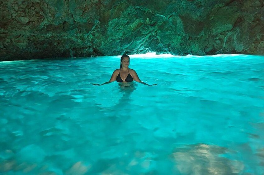 A person in a black swimsuit in clear turquoise water, surrounded by rocky cave walls. 1