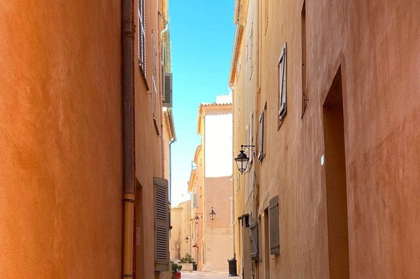 A narrow street flanked by buildings with shutters and a clear blue sky. 4
