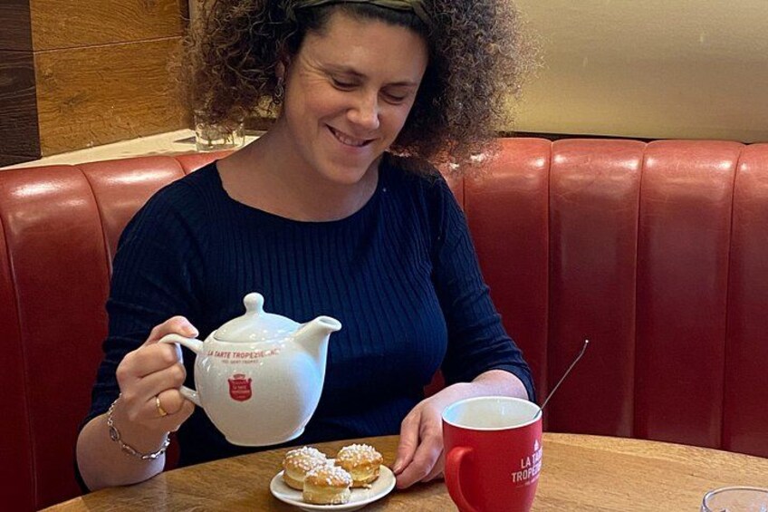 A person sitting at a table with a teapot, a cup, and a plate of pastries. 1