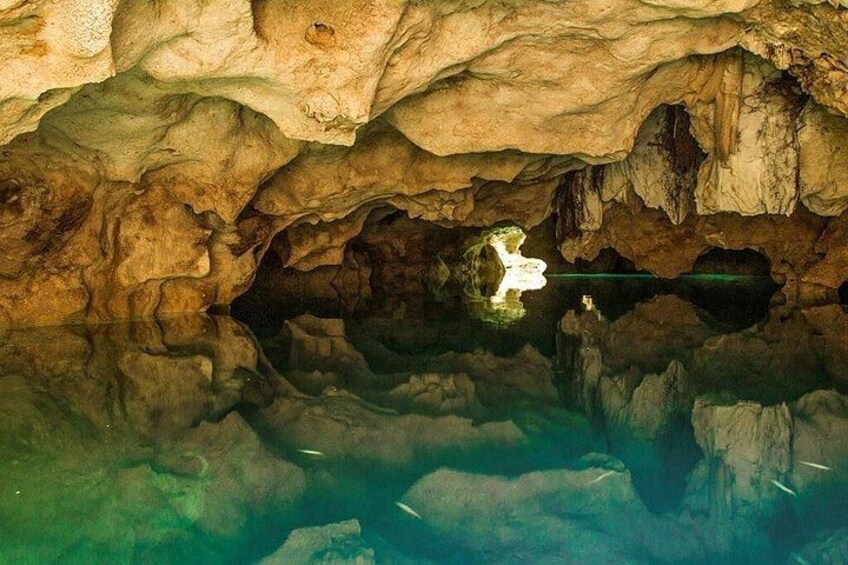 L’intérieur d’une grotte, avec des stalactites et des stalagmites, une eau claire et une source de lumière qui se reflète à la surface de l’eau. 3
