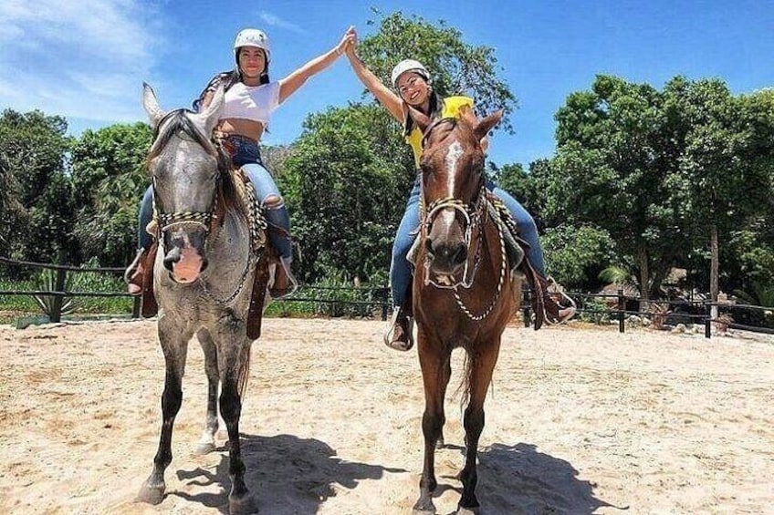 Two people riding horses in an outdoor arena with trees in the background. 3