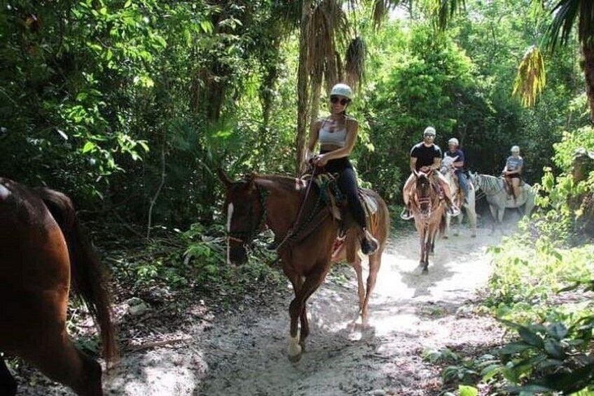 A group of people riding horses on a dirt path through a forested area. 2