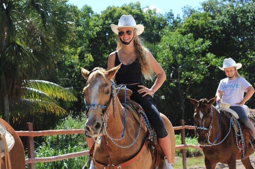 Two people riding horses in a fenced area with trees in the background. 4