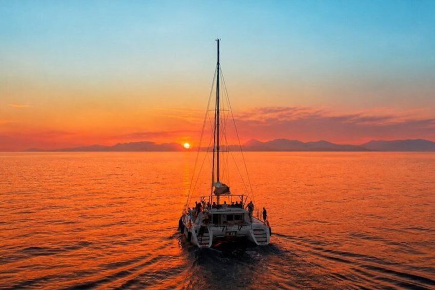 A sailboat on calm waters during sunset with a clear sky and distant mountains. 1