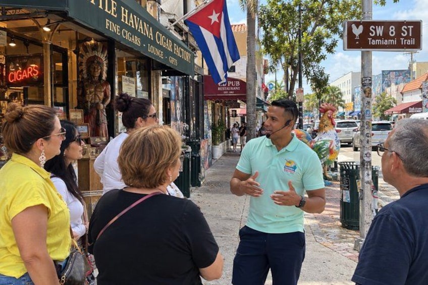 A street scene with people standing and talking, storefronts, and a Cuban flag. 5