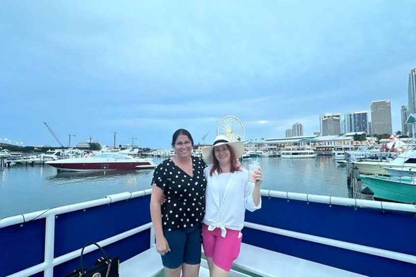 Dos personas en un barco con un puerto deportivo y un horizonte urbano de fondo. 2