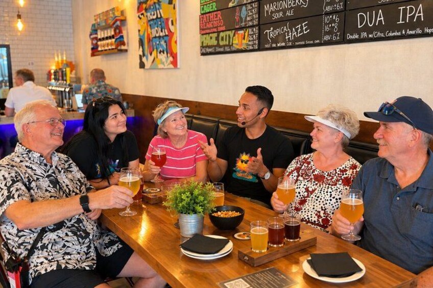 A group of people sitting at a wooden table in a restaurant, holding glasses of beer. 4