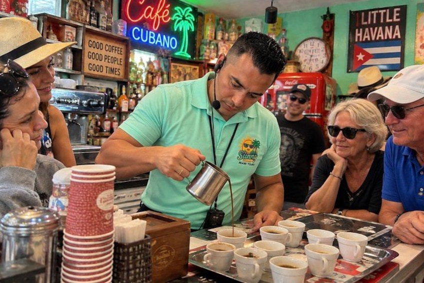 A barista preparing coffee at a counter with a sign that reads 'Café Cubano' and 'Good Coffee, Good People, Good Times.' 3