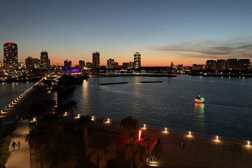 Un paisaje urbano frente al agua al anochecer, con edificios iluminados y un barco en el agua. 2