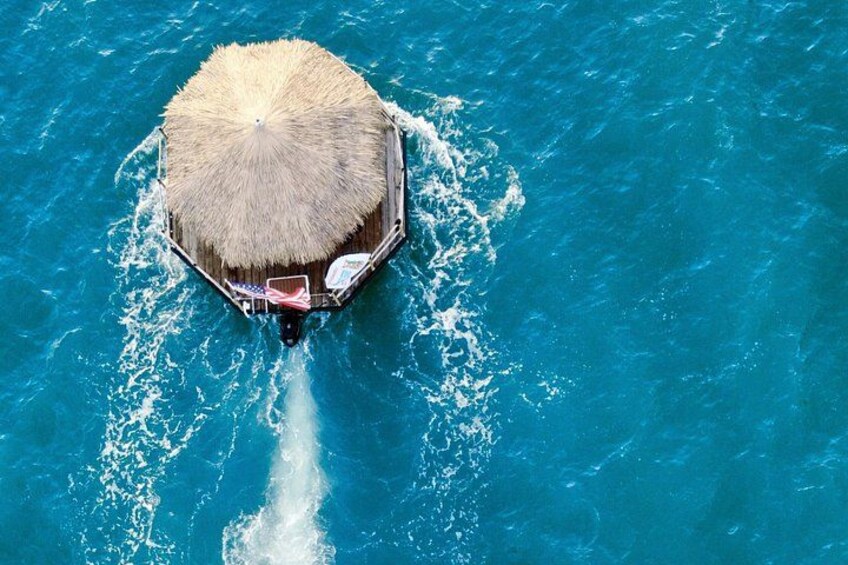 Una cabaña sobre el agua con techo de paja, rodeada de aguas turquesas. 4