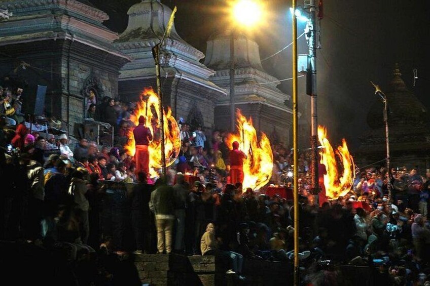 A nighttime outdoor event with large flames, a crowd, and traditional architecture. 3