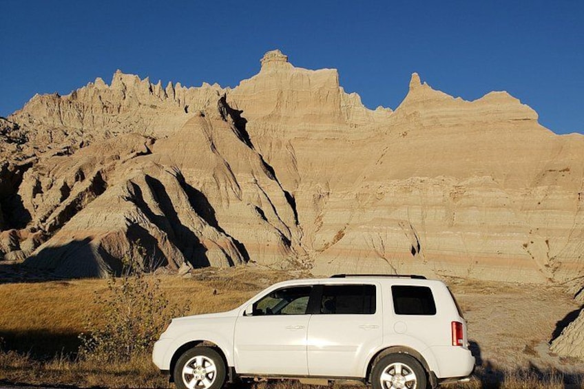 Un SUV blanco estacionado en un campo, con una extensa y escarpada cadena montañosa al fondo. 1