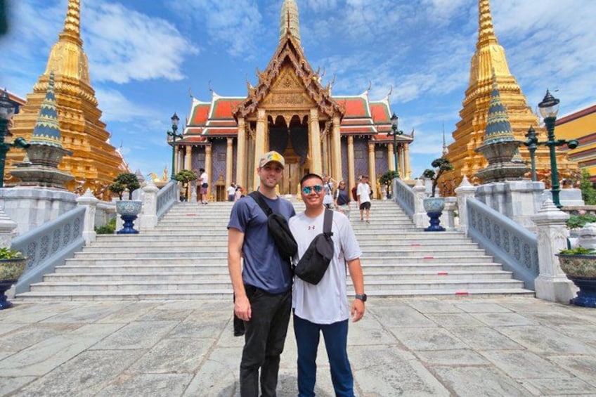 Two people standing in front of a temple with a staircase leading up to it. 1