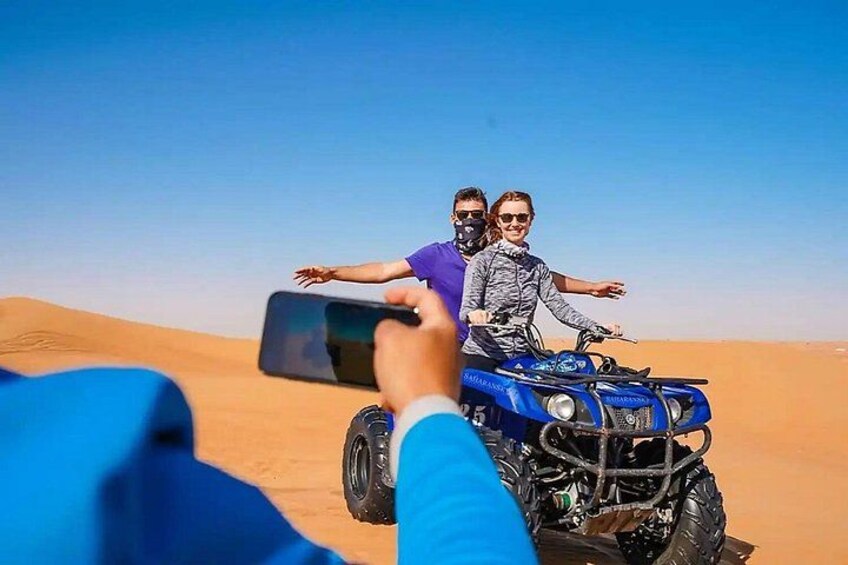 Zwei Personen in einem blauen Geländewagen in einer Wüste mit Sanddünen. 1