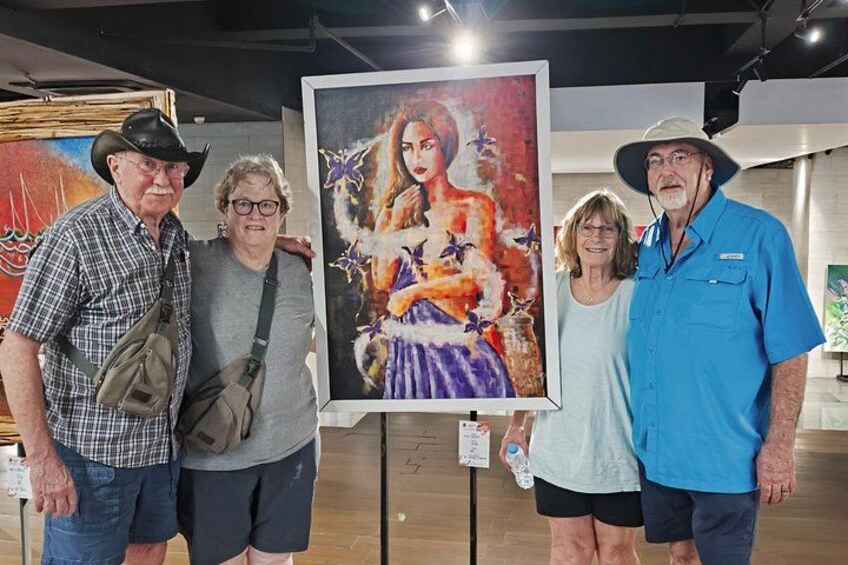Four people standing in an art gallery with a large painting of a woman in a dress. 2