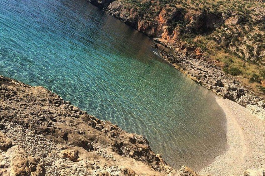Eine Küstenlandschaft mit klarem türkisblauem Wasser, felsigem Gelände und einem Sandstrand. 5