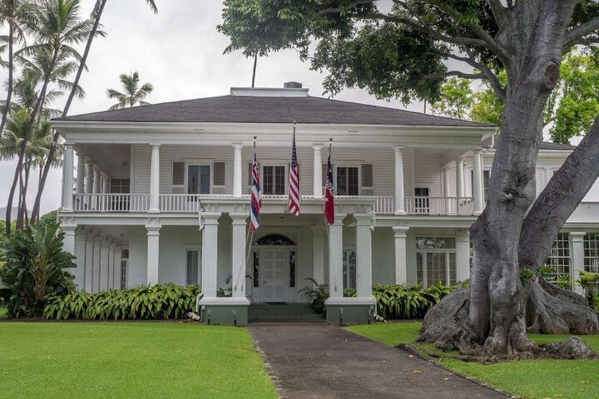 Un edificio de estilo colonial blanco con un porche, dos banderas y un gran árbol en primer plano. 3