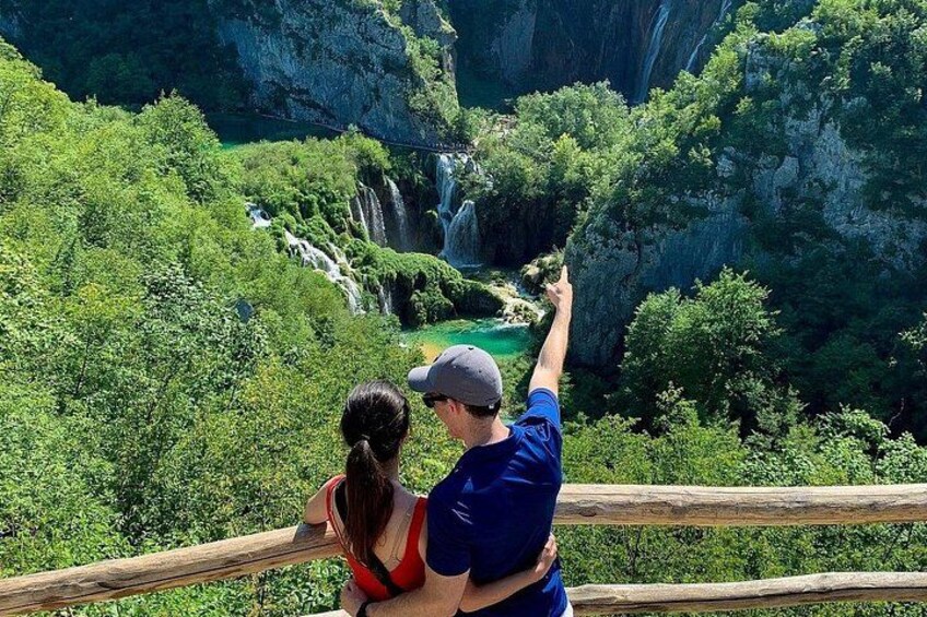 Una pareja observa una cascada rodeada de exuberante vegetación y acantilados rocosos. 3