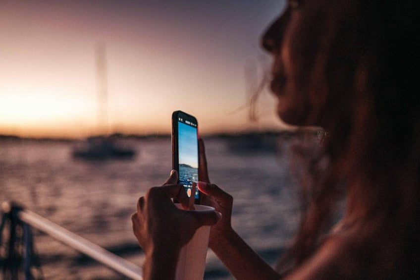 Une personne tenant un téléphone intelligent, avec un coucher de soleil en arrière-plan. 3