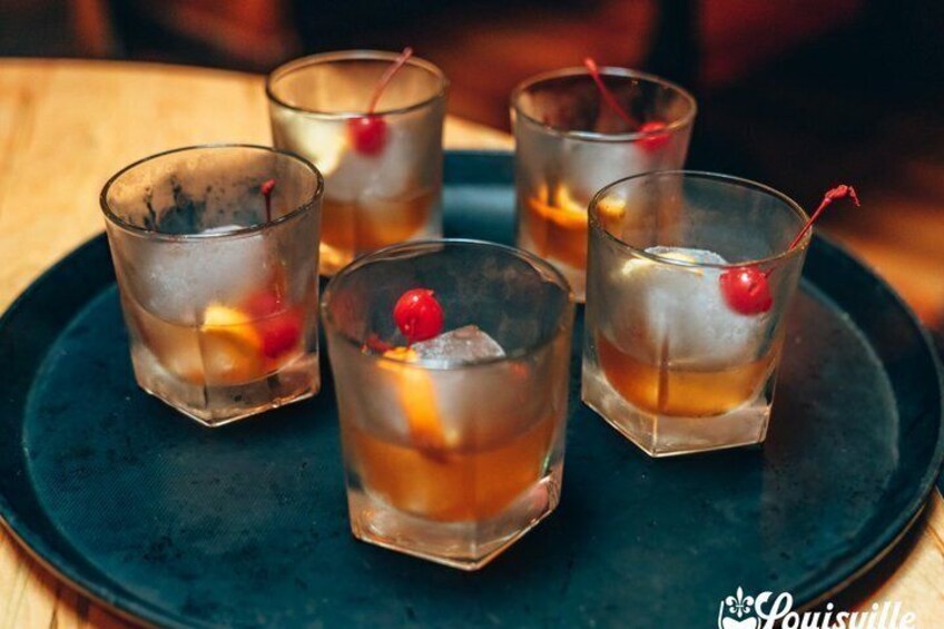 Four glasses of a dark beverage with fruit and a cherry on a dark plate. 3