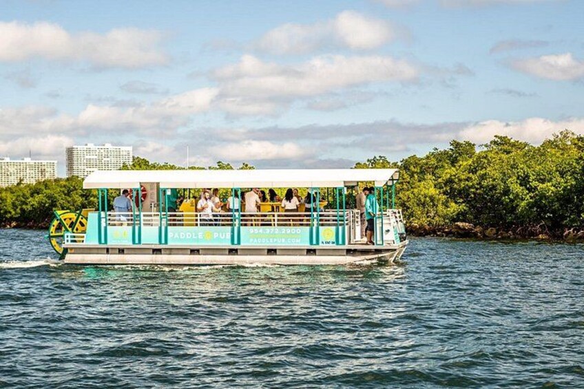 A paddle boat with people on it, moving on water with a cityscape in the background. 2