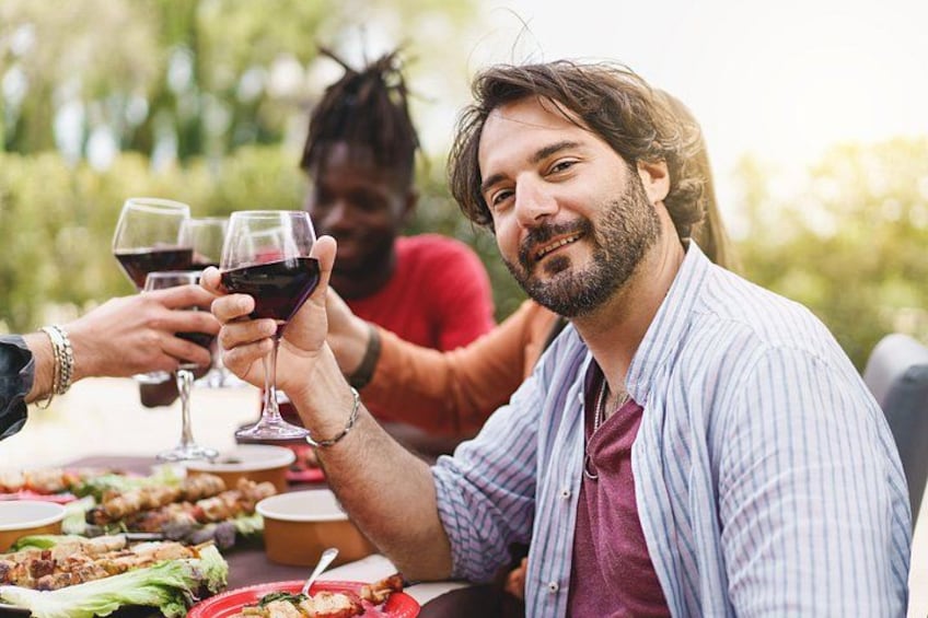 Un grupo de personas brindando con copas de vino en una mesa al aire libre con comida. 5