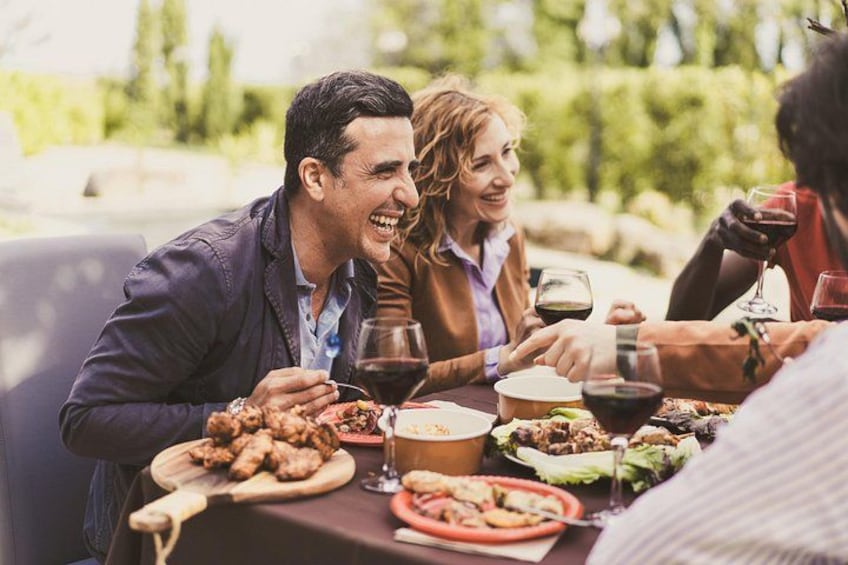 Un grupo de personas cenando al aire libre en una mesa con diferentes platos y bebidas. 4