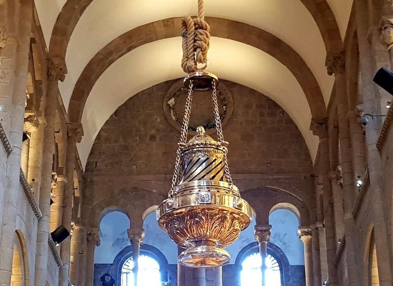 A large, ornate chandelier hanging from a high arched ceiling in a historic building with stone columns and arches. 1
