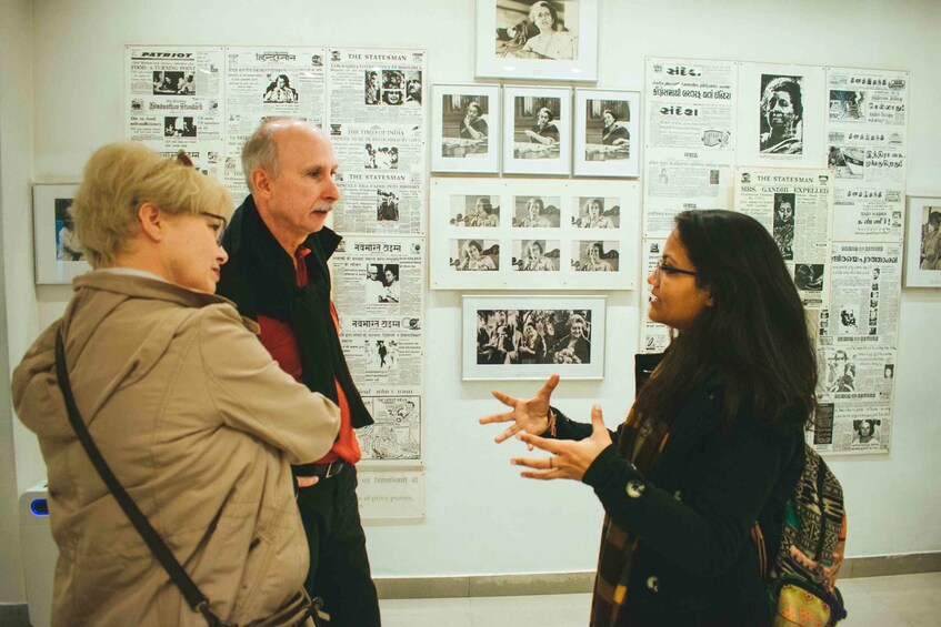 Three people in a museum with photographs and newspaper clippings on the wall. 1