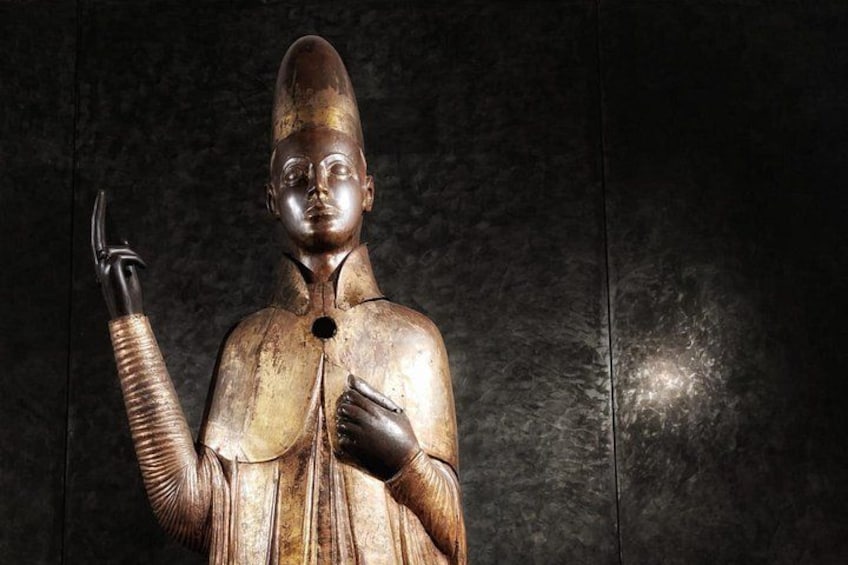 A bronze statue with a pointed hat, raised right hand, and a clenched left fist. 3