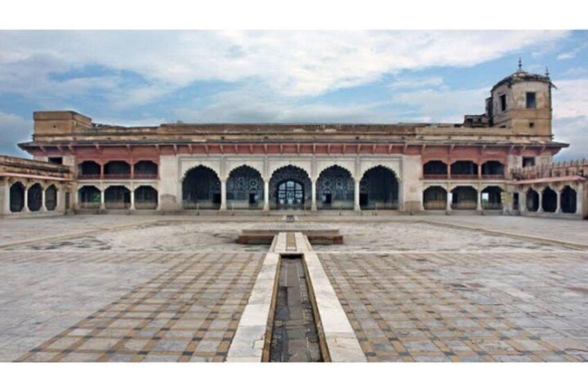 Une vaste cour intérieure avec un canal d’eau central, entourée d’arcades et bordée d’un bâtiment doté d’une tour. 3
