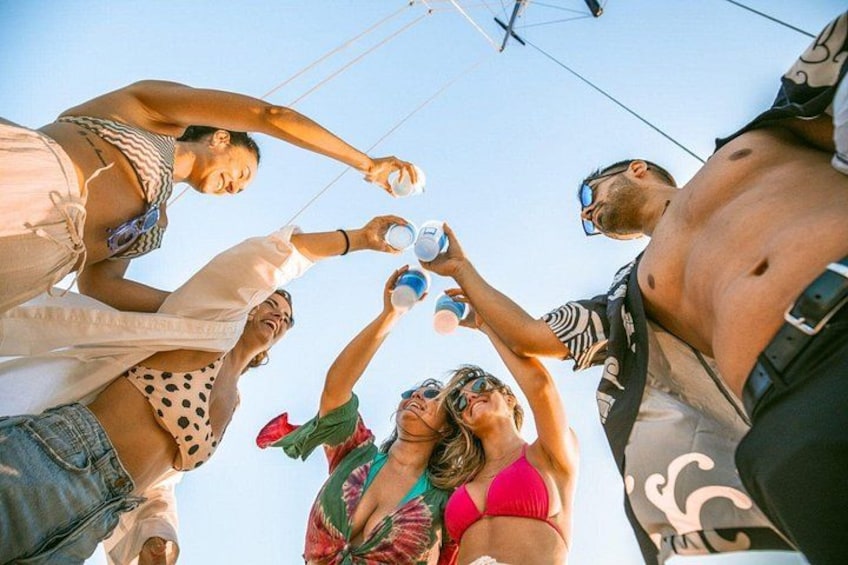 A group of people toasting with cups, a clear sky, and a boat in the background. 3