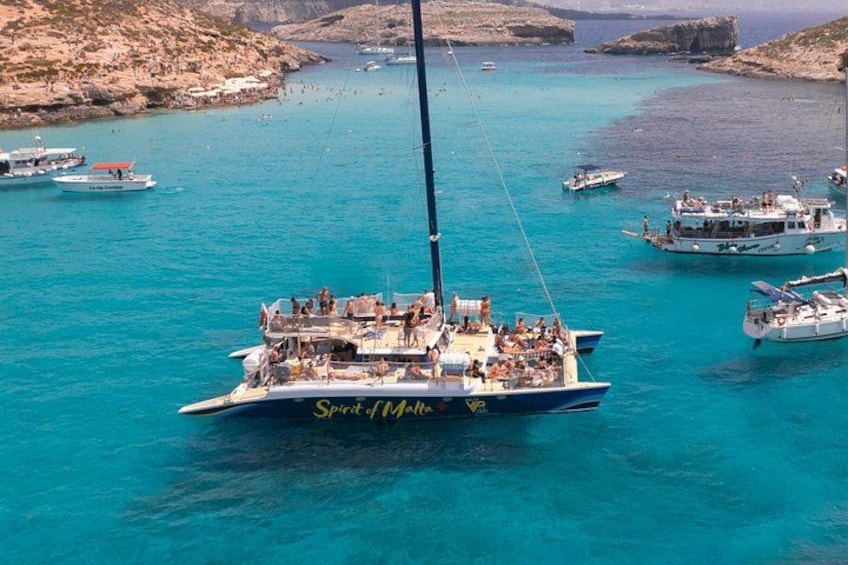 En sejlbåd, der hedder 'Spirit of Malta', med passagerer, omgivet af rolige turkisblå farvande og klippekyst. 3
