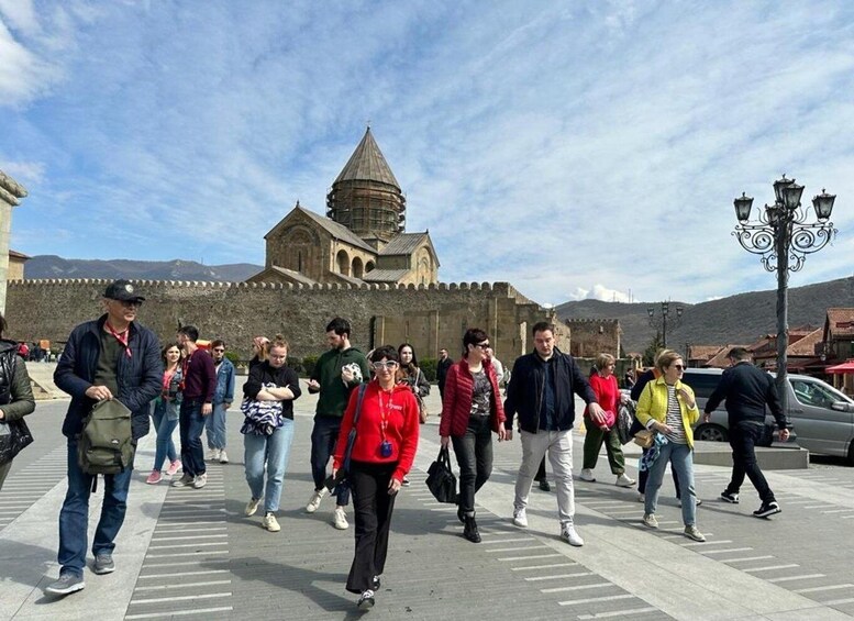 A group of people walking in a pedestrian area with a historic building featuring a dome and arches in the background. 2