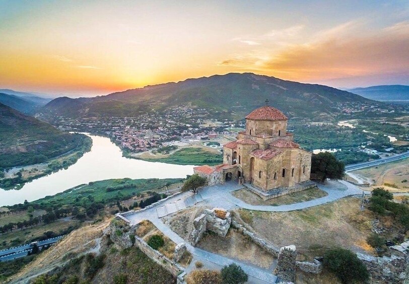 A historic church with a dome, surrounded by a valley and a river, with mountains in the background. 1