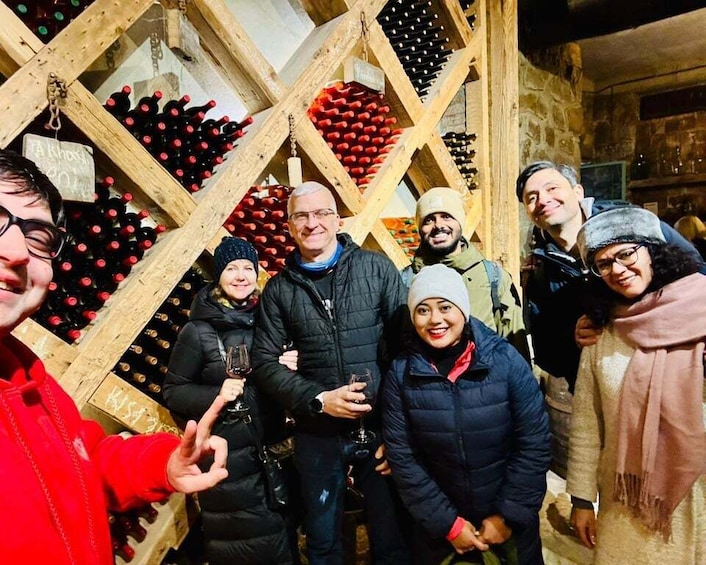A group of people in a wine cellar with wooden racks of wine bottles. 4