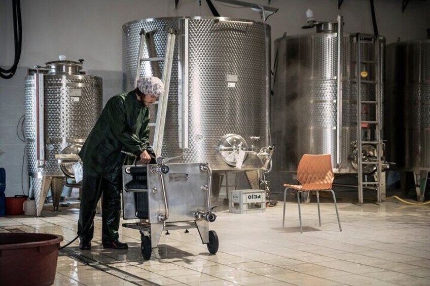 En person i labbrock som manövrerar en vagn i ett rum med tankar av rostfritt stål. 4
